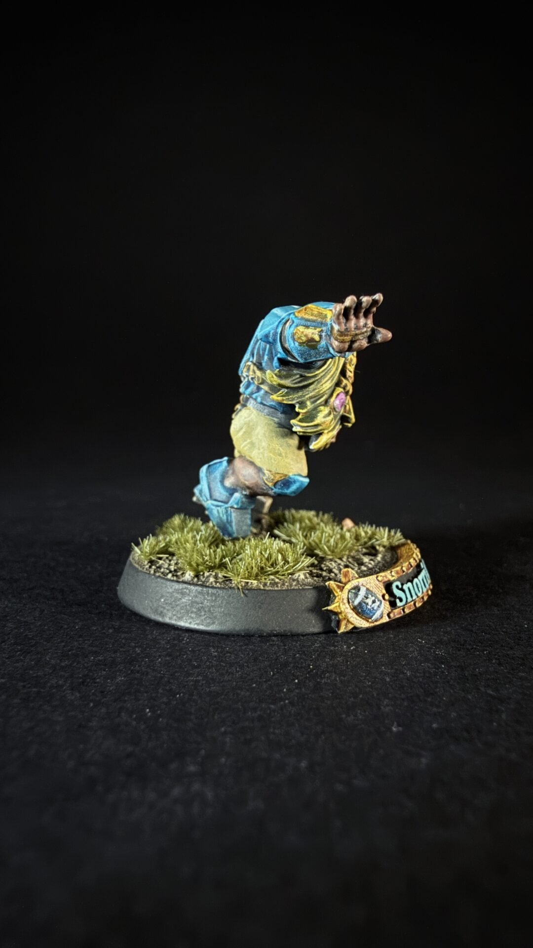 Painted tabletop mini figure of a blue-and-yellow armored character raising its arm, mounted on a grassy base with a banner reading 'Snow' nearby.