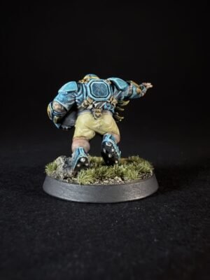 Back view of a blue armored miniature charging forward on a grassy, rocky base.