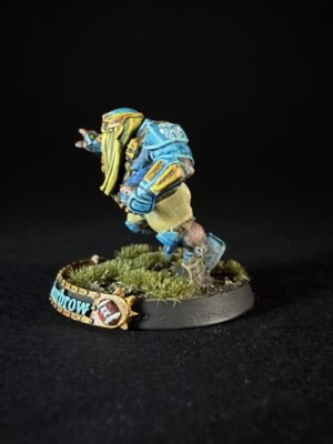 Painted miniature sci‑fi armored warrior in blue and yellow standing on a grassy base.
