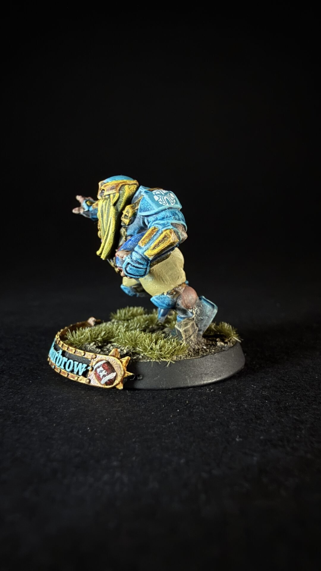 Painted miniature sci‑fi armored warrior in blue and yellow standing on a grassy base.