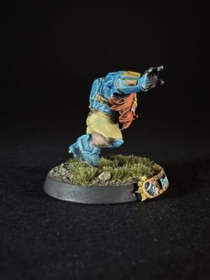 Miniature fantasy figure in blue armor jumping forward on a grassy, rocky base against a black background.