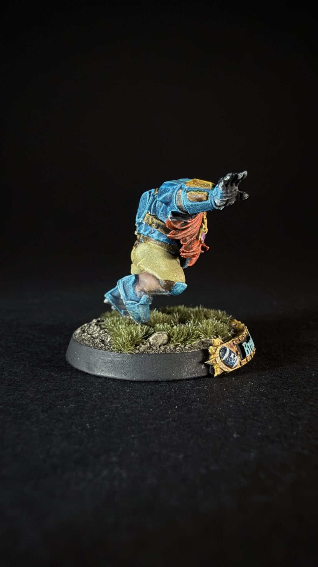 Miniature fantasy figure in blue armor jumping forward on a grassy, rocky base against a black background.