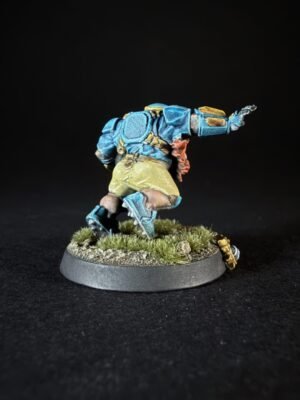 Painted sci‑fi miniature in blue armor leaping forward on a grassy base, with a brown belt and red sash detail against a black backdrop.