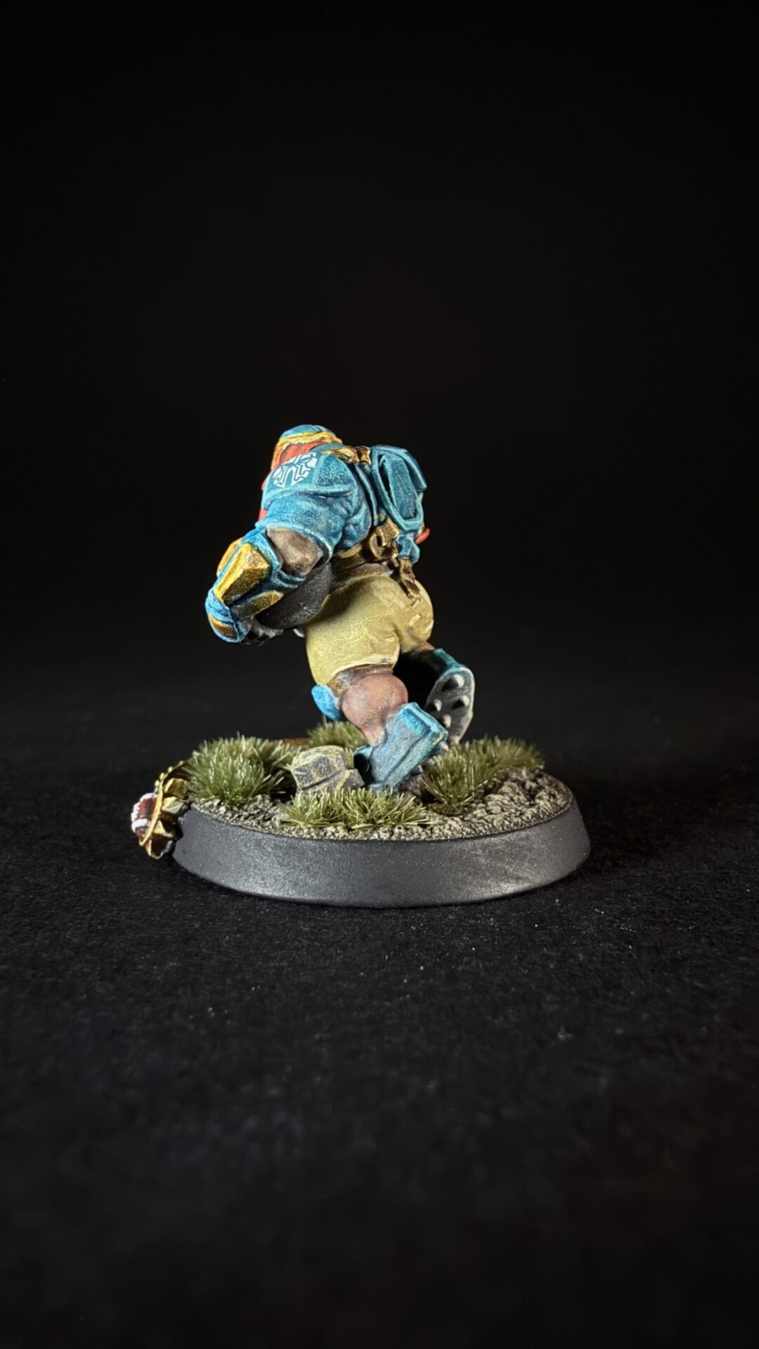 A painted fantasy miniature of a bearded warrior in blue armor sprinting across a grassy base on a round stand
