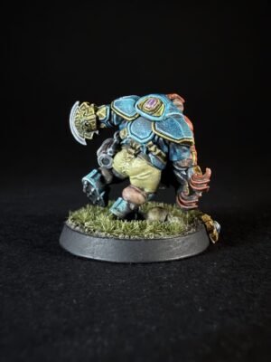 Back view of a painted fantasy miniature in blue armor with yellow trim, standing on a grassy base with a circular axe-like weapon nearby.