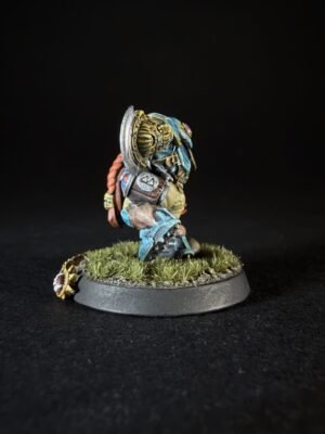 Miniature warrior with blue armor and red hair, holding a shield, standing on a grassy base against a dark background.