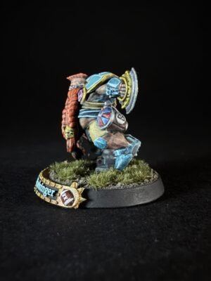Painted fantasy miniature of a blue-armored warrior with a round shield, charging forward on a grassy base.