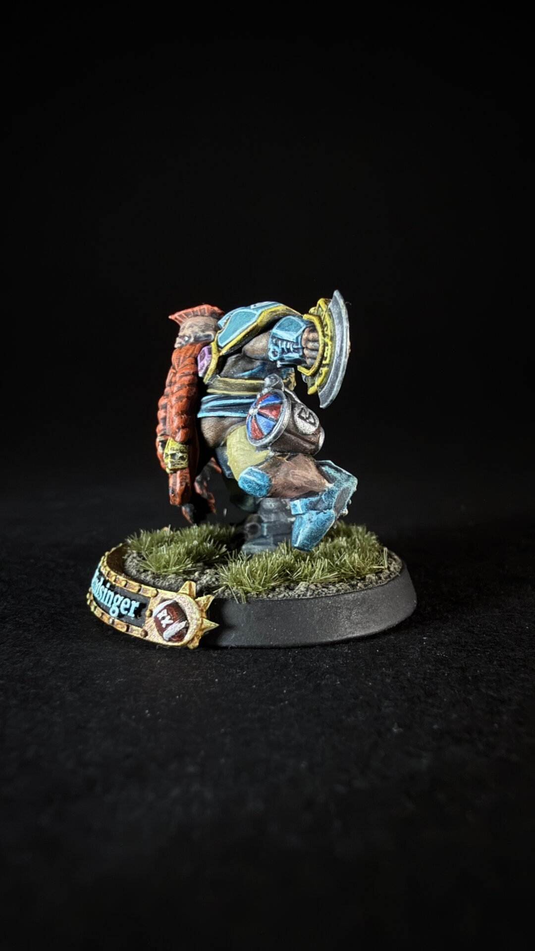 Painted fantasy miniature of a blue-armored warrior with a round shield, charging forward on a grassy base.