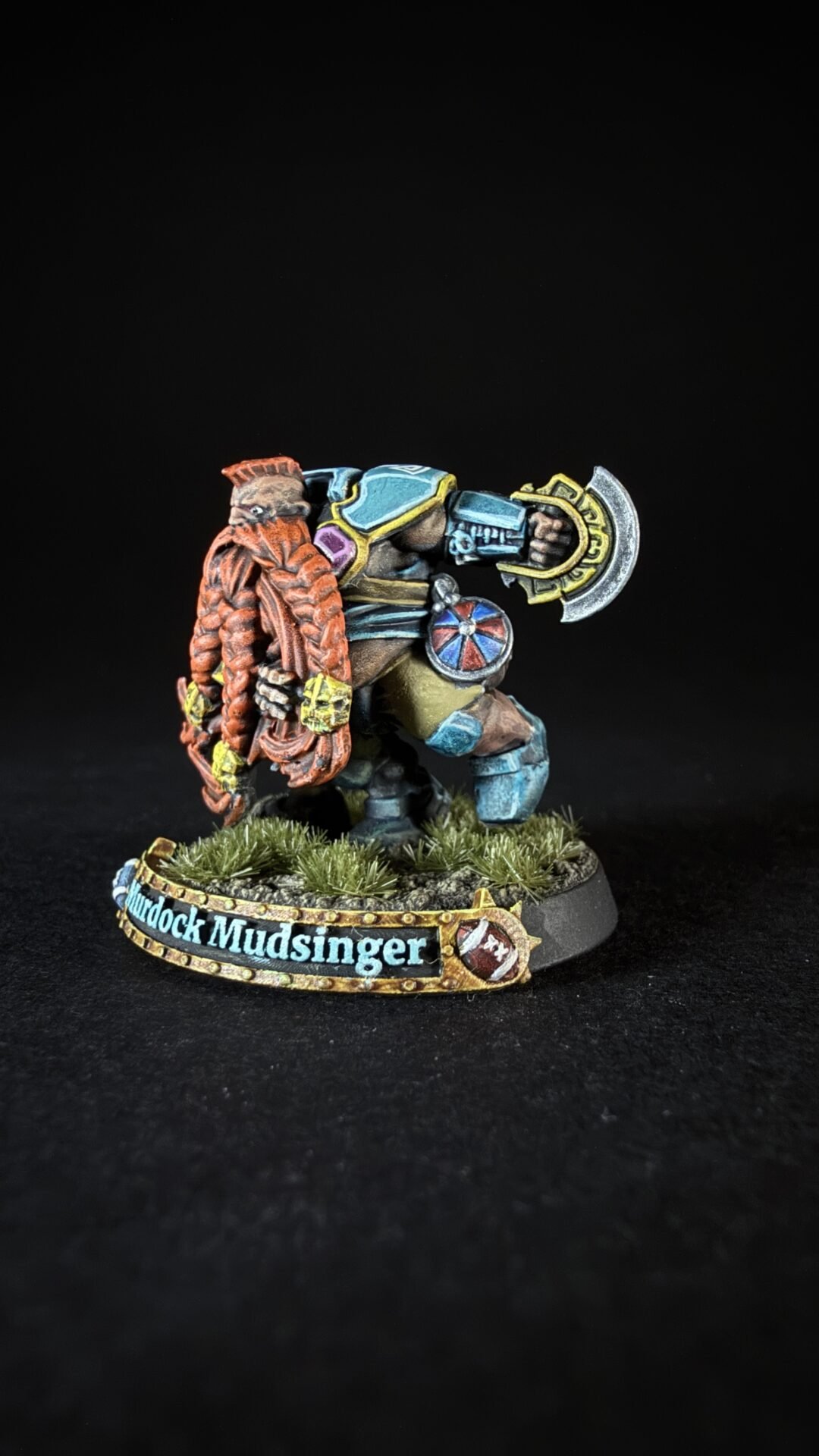 Colorful fantasy dwarf miniature in blue armor, gripping a large battle axe, on a grassy diorama with a name banner on the base.