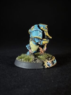 Small fantasy miniature figurine in blue armor with yellow trim, standing on a grassy diorama base against a black background.