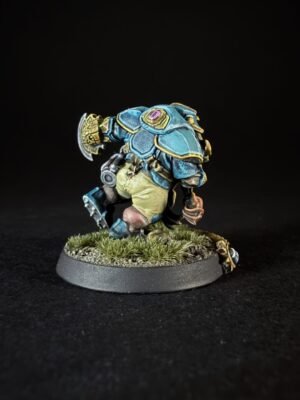 Painted fantasy miniature: a blue armored warrior with gold trim and a purple gem, standing on a grassy base.