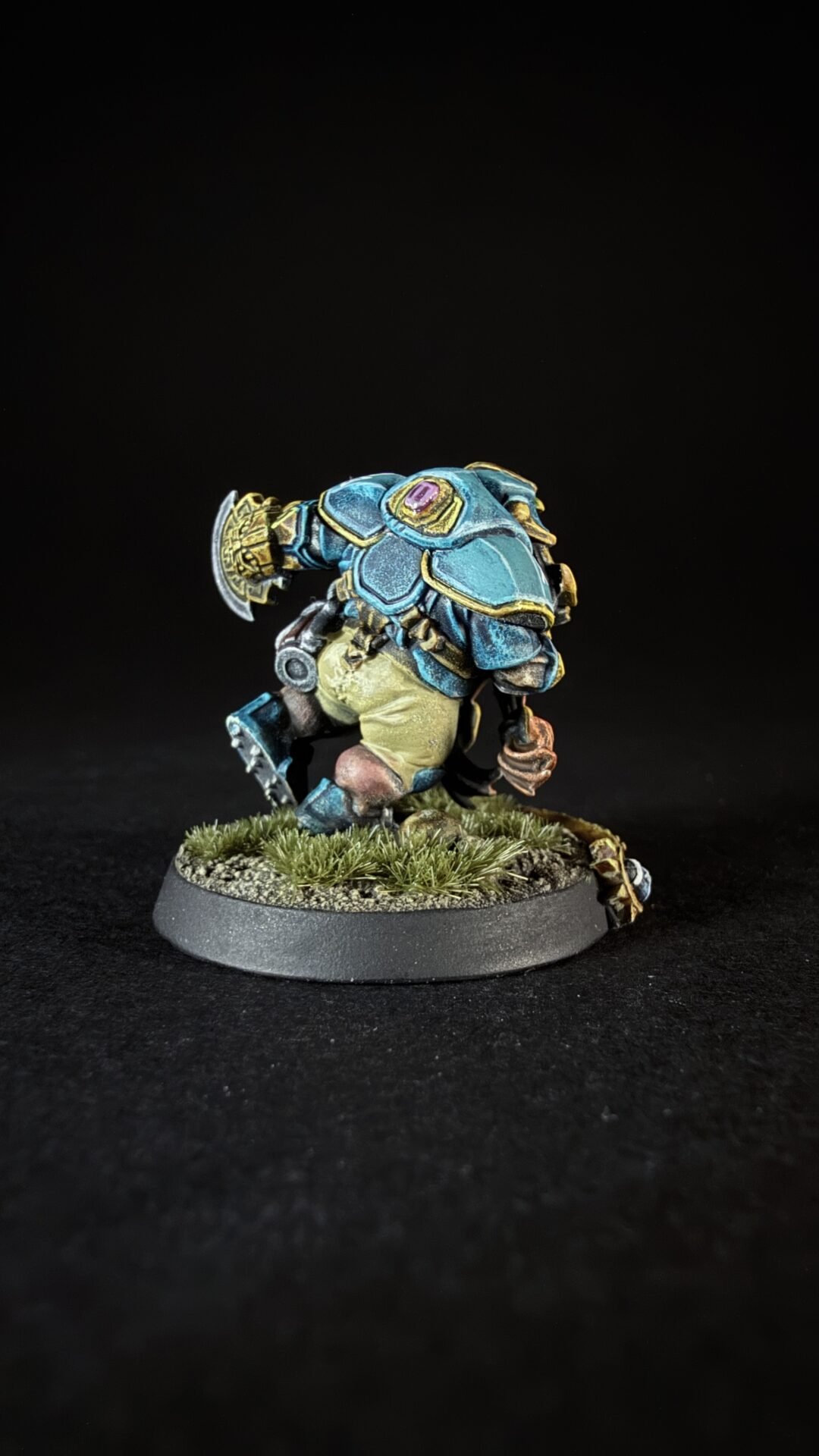 Painted fantasy miniature: a blue armored warrior with gold trim and a purple gem, standing on a grassy base.