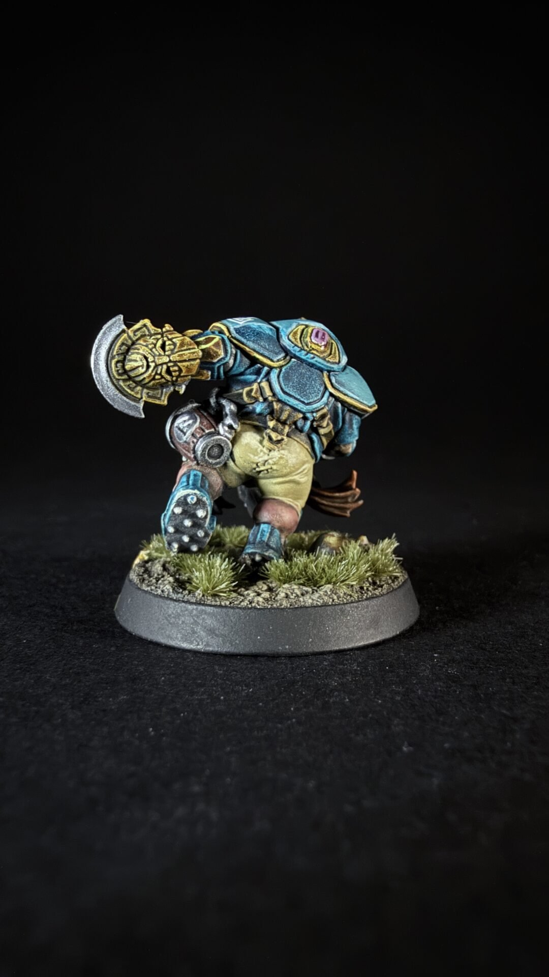 Painted fantasy dwarf miniature in blue armor with a large ornate hammer, standing on a grassy battlefield base.