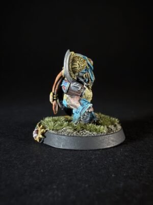 Side-view of a painted fantasy dwarf warrior with blue armor, shield, and axe on a grassy diorama base.