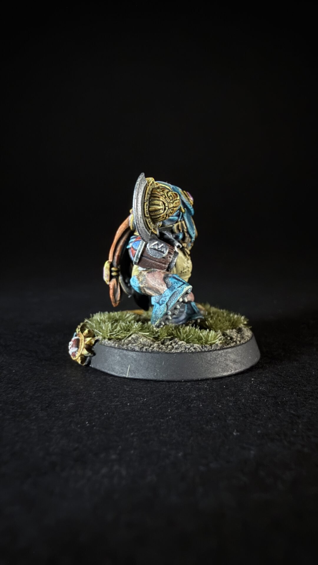 Side-view of a painted fantasy dwarf warrior with blue armor, shield, and axe on a grassy diorama base.