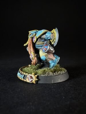 Colorful painted fantasy miniature of a heavy-armored warrior with a round shield and axe, standing on a grassy diorama base.
