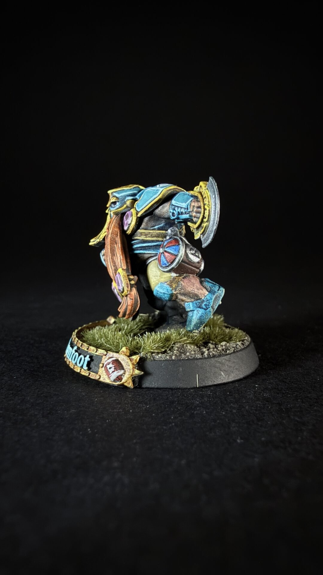 Colorful painted fantasy miniature of a heavy-armored warrior with a round shield and axe, standing on a grassy diorama base.