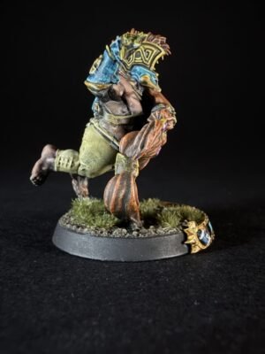 Colorful fantasy orc miniature charging forward, armed with a blue-and-gold shield, on a rocky grassy base.
