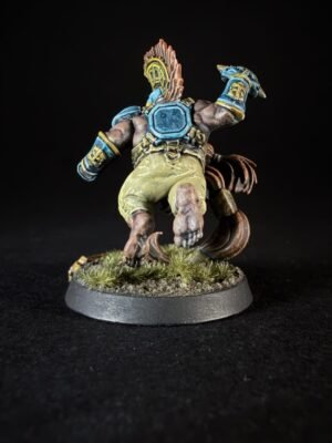 Back view of a painted fantasy miniature: muscular figure in blue armor with a feathered crest, tan shorts, and dynamic pose on a grassy base.