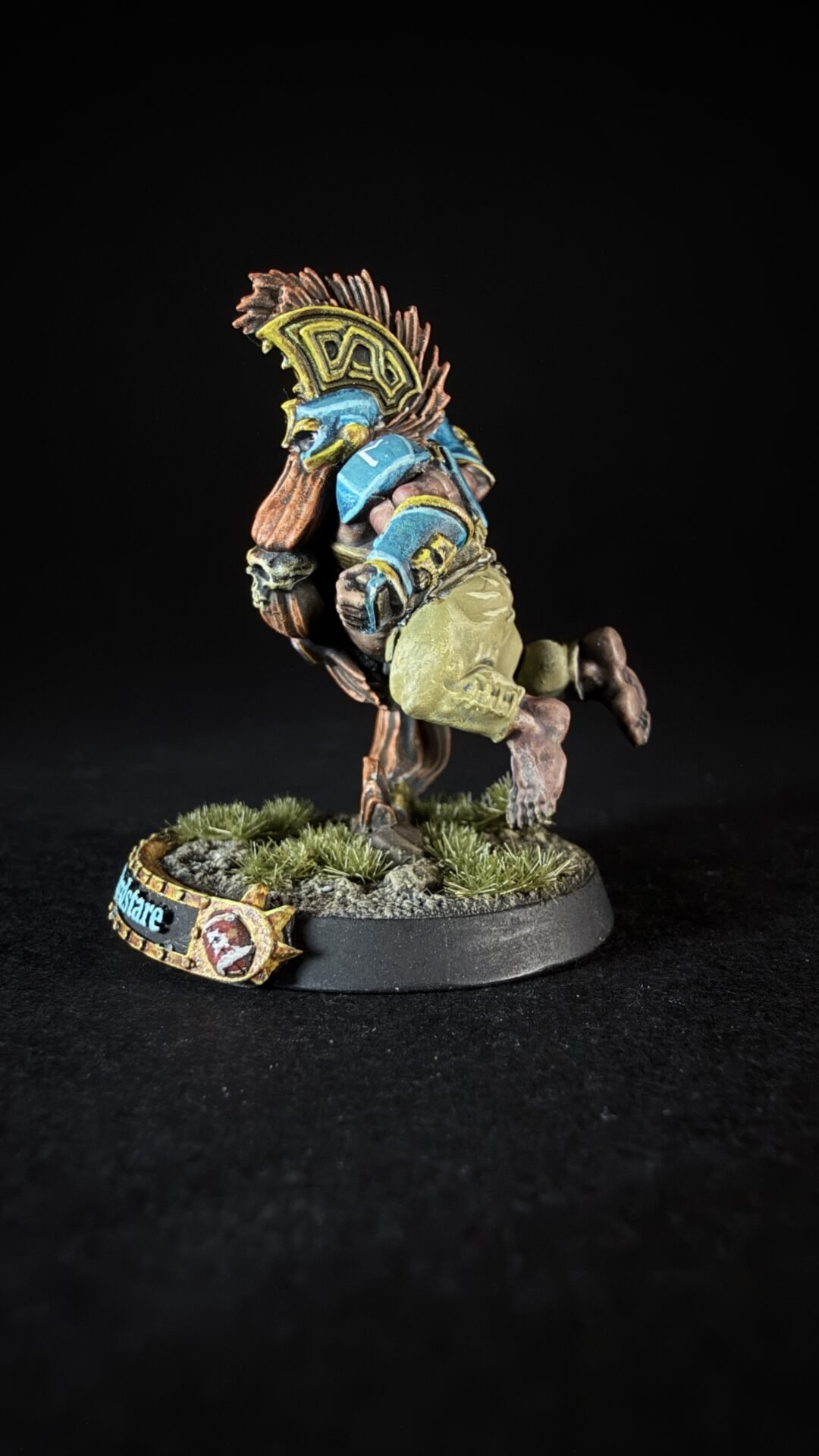 Painted fantasy miniature of a warrior running, wearing a blue and yellow winged helm with brown hair and armor, on a grassy textured base.