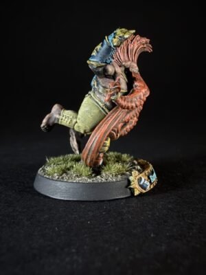 Painted tabletop miniature of a rider on a red dragon-like creature, on a grassy base against a black background.