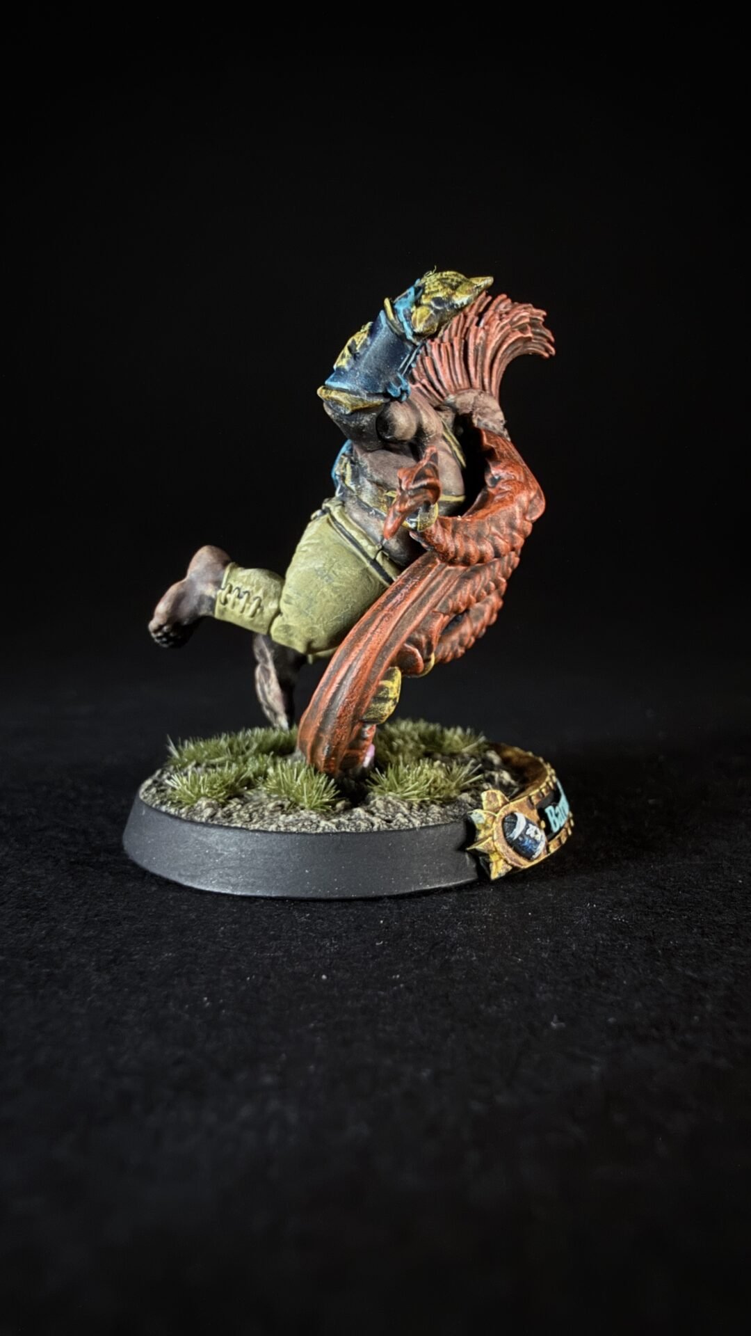Painted tabletop miniature of a rider on a red dragon-like creature, on a grassy base against a black background.