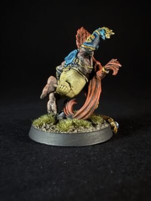 Painted fantasy miniature on a round base, humanoid figure in blue and gold armor with a red cloak, posed in an action stance on a grassy, rocky base.