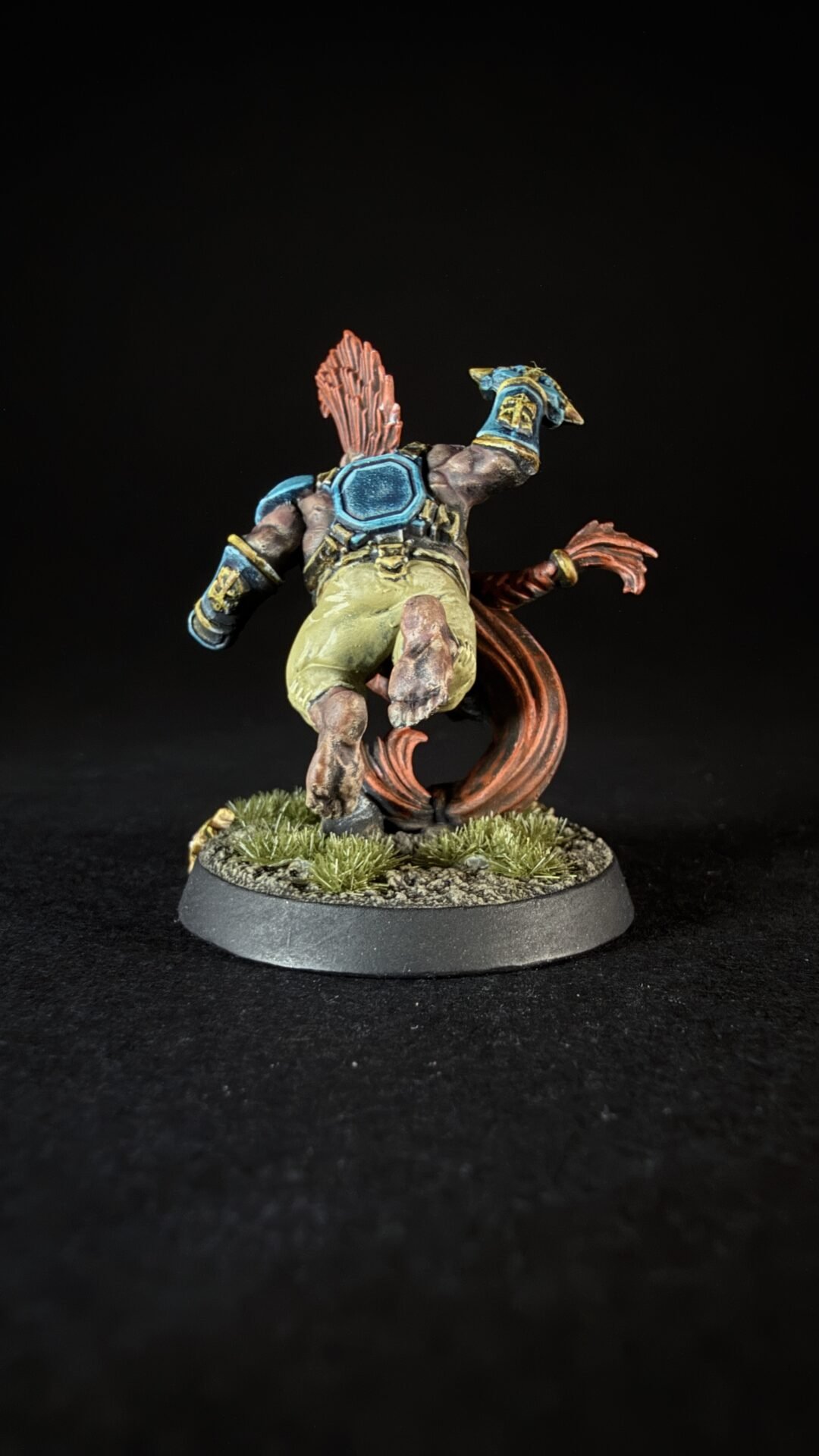 Back view of a fantasy miniature: armored figure sprinting with a blue chest plate, teal gauntlets, and a red energy trail behind, on a grassy base.