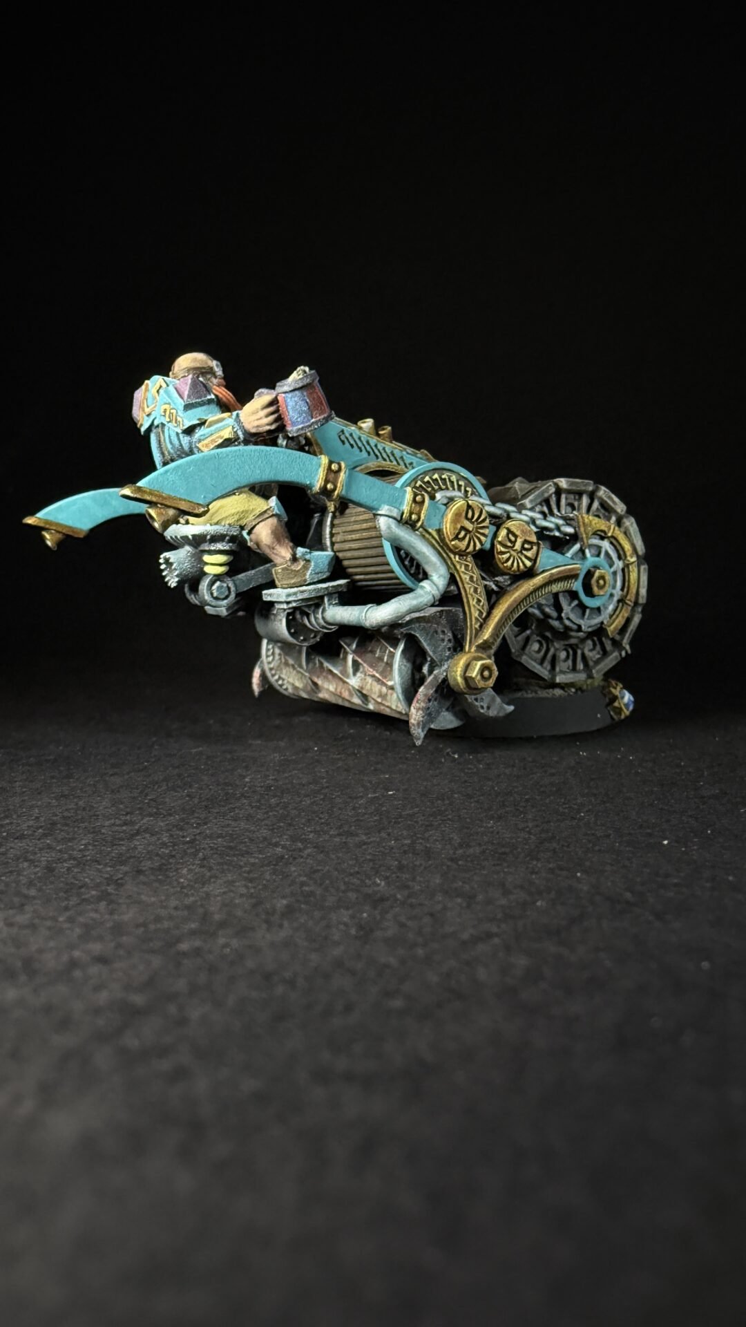 Miniature steampunk motorcycle with teal and gold gears and a rider, set against a black background.
