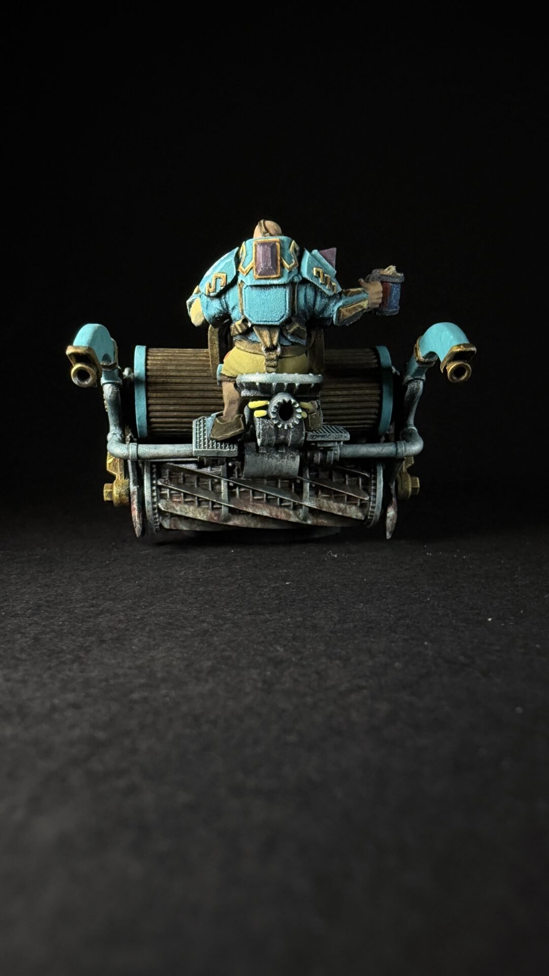 Teal and gold armored sci‑fi soldier sits atop a weathered dieselpunk vehicle with pipes and gears against a black background.