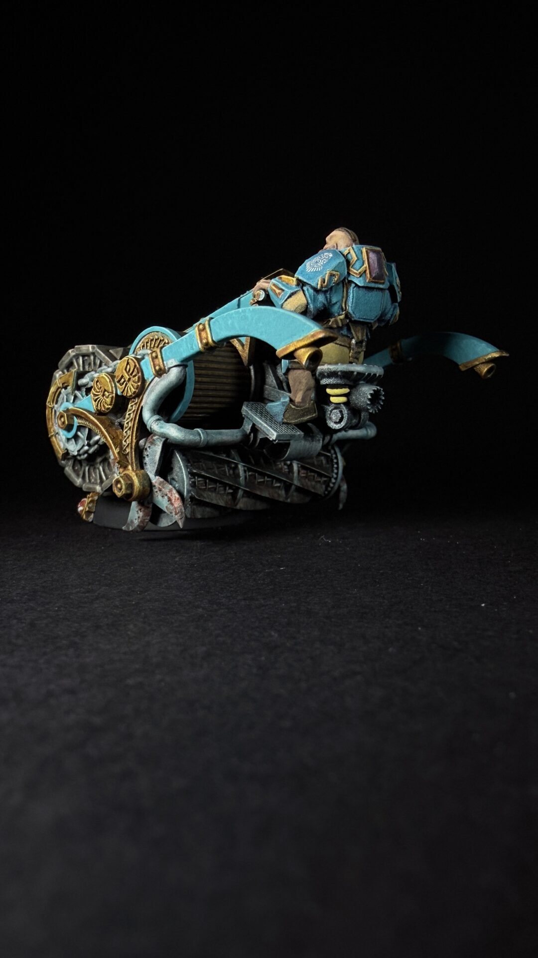 Steampunk blue-and-gold motorcycle with a armored rider on a dark background, close-up profile view.