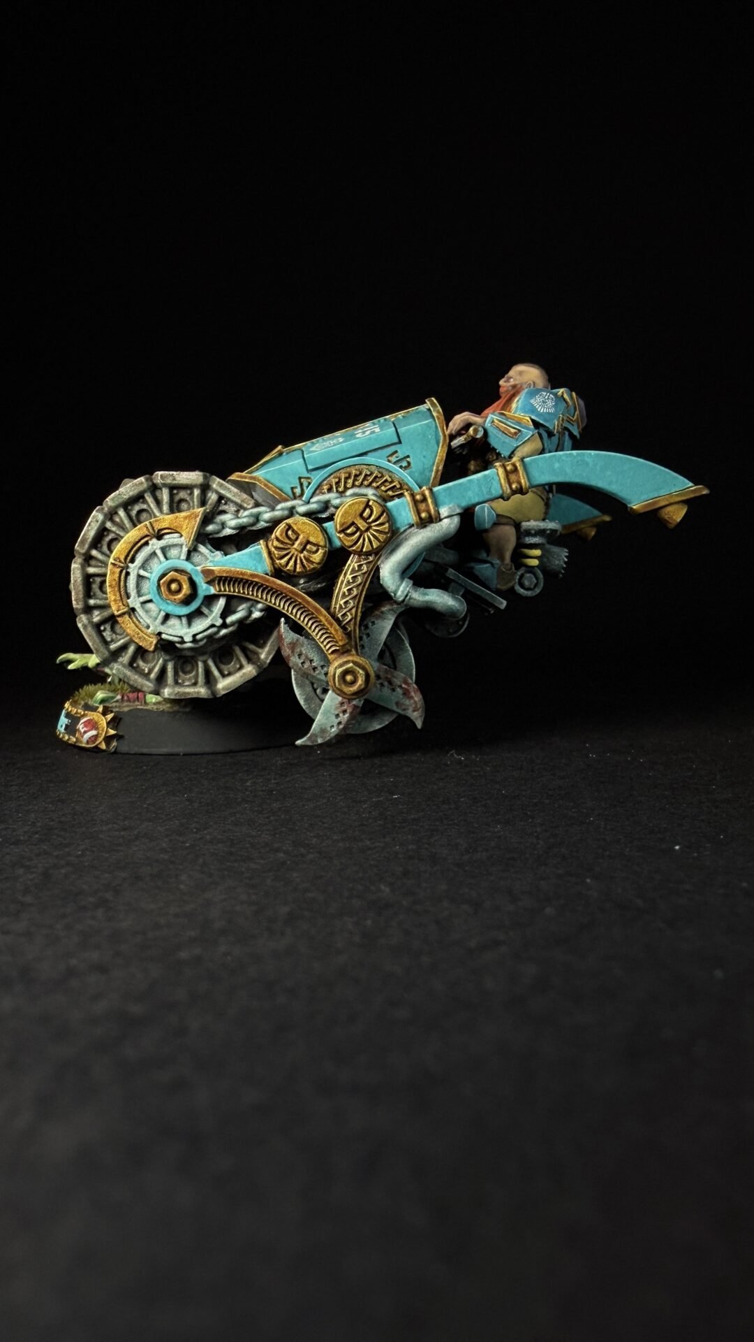 Teal and gold steampunk motorcycle model with large gear wheel and ornate gears, carrying a rider in armor.