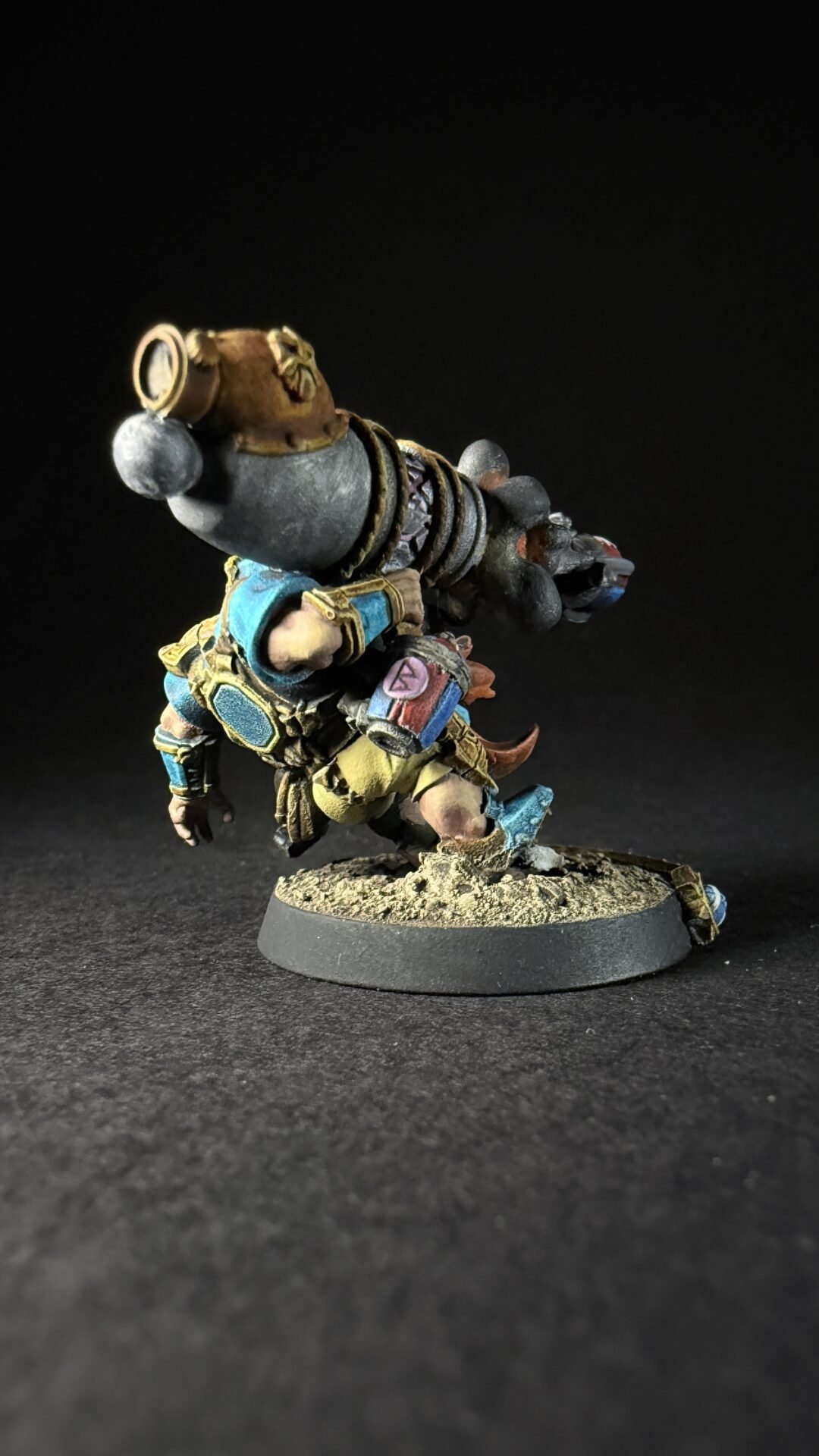 Painted fantasy dwarf miniature with a large back-mounted cannon, wearing blue and gold armor on a rocky base.