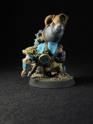 IMG_1123 Back view of a small fantasy dwarf in blue and gold armor, standing on a rocky base against a black background. The figure is detailed with plates, straps, and a helmet-like headpiece, presenting a heroic, armored silhouette.