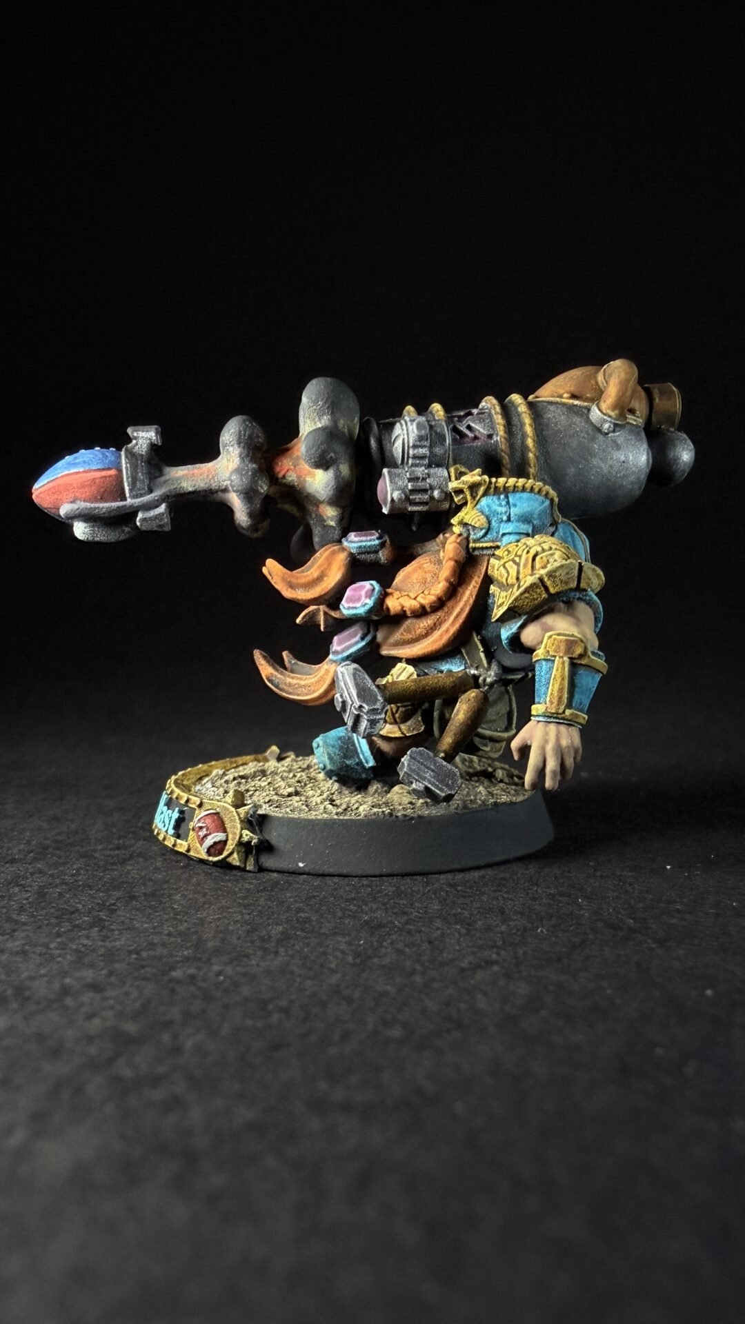 Painted miniature of a horned dwarf/warrior in blue and gold armor, wielding a large hammer with a ram-like siege device on its back, standing on a textured base.
