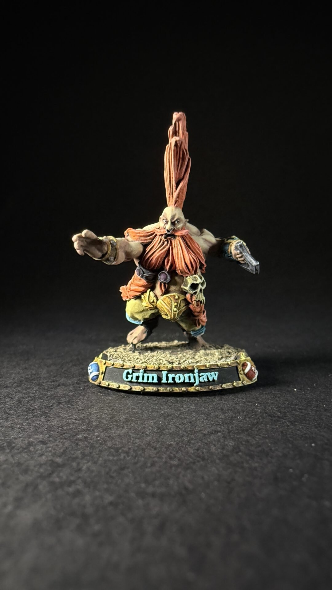 Miniature dwarf figure Grim Ironjaw with a tall orange beard, muscular build, armor, and outstretched arms on a rocky base.