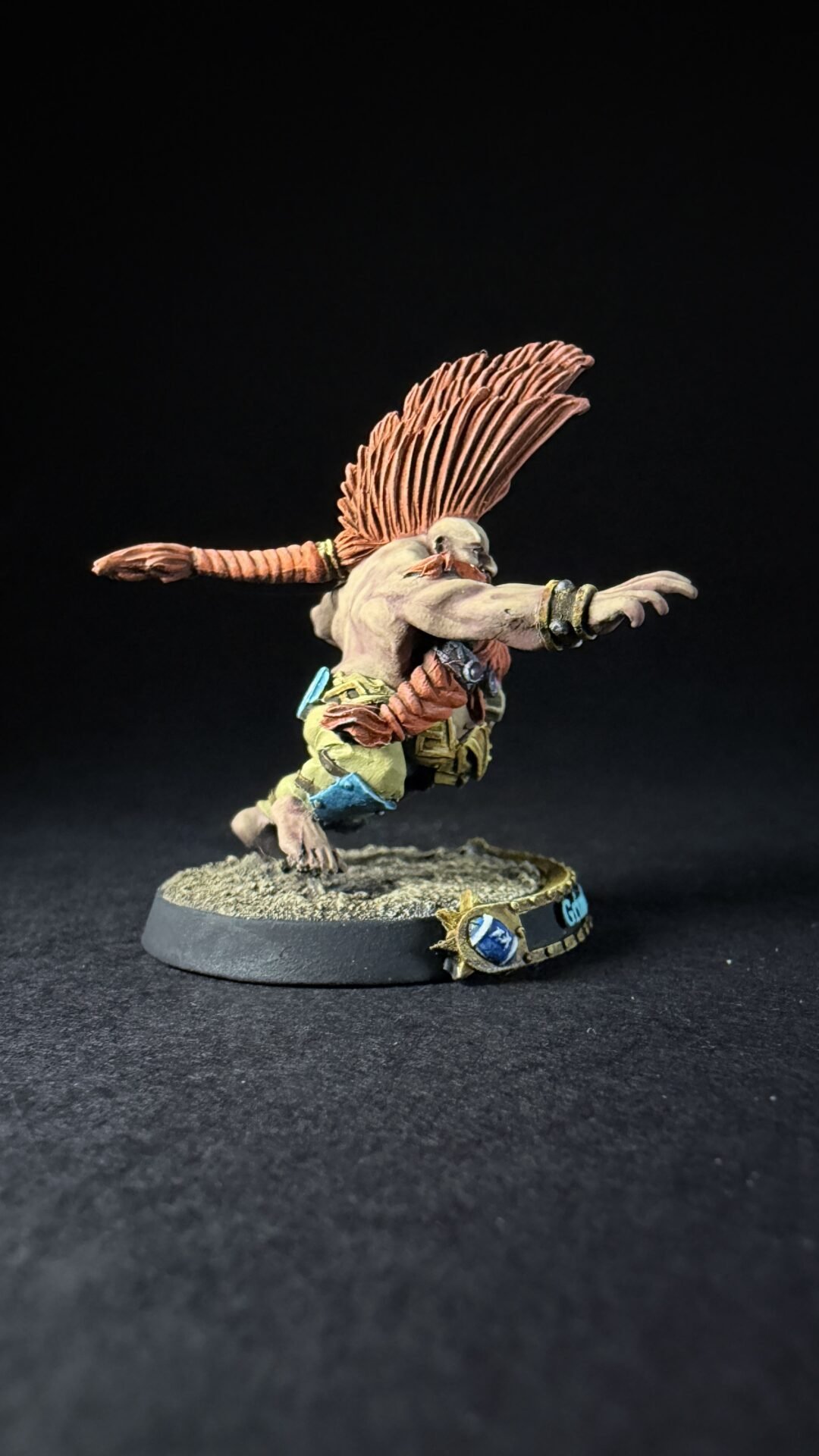 Winged humanoid miniature sprinting forward with orange feathered wings, wearing rugged armor on a textured diorama base.