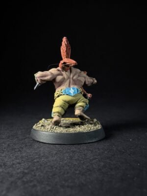 Back view of a miniature figure with orange hair tied in a plume, wearing olive pants and a blue belt on a rocky base against a dark background