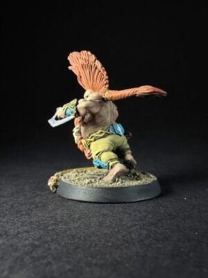 Miniature fantasy figure with orange feathered crest, muscular torso, green pants, and a curved blade, posed on a rocky base.