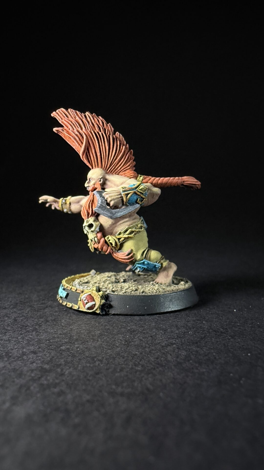 Fantasy miniature figure of a winged humanoid warrior mid-leap, with orange plumage headdress and armor, on a rocky base.