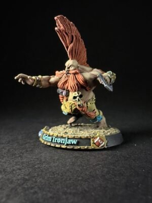 Fantasy orc warrior miniature with a tall orange mohawk, skull belt, and outstretched arms on a textured base reading 'Glin Ironjaw'.