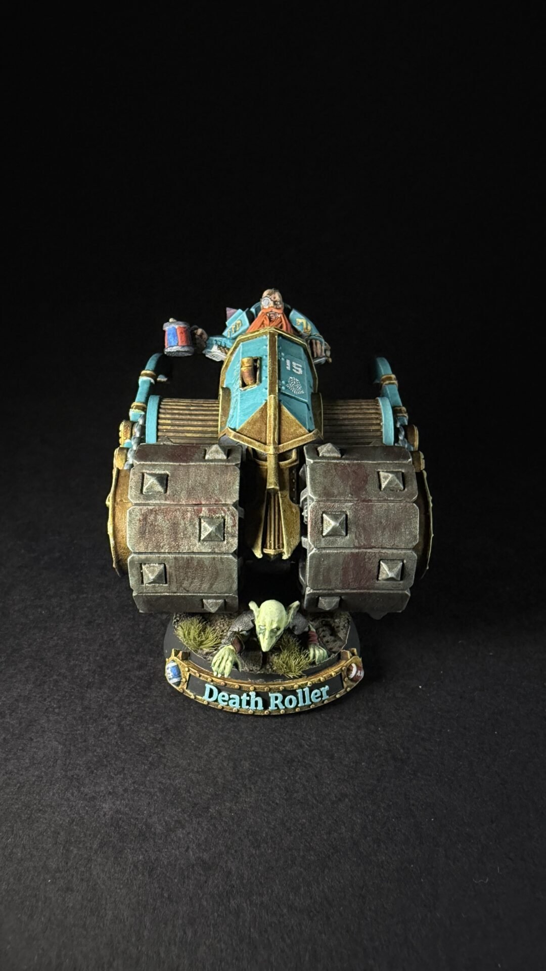 Miniature model of a teal and gold Death Roller siege vehicle with large treaded wheels and a goblin pilot, set against a black background; base reads 'Death Roller'.