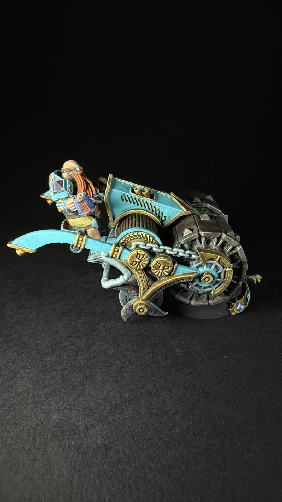 Miniature fantasy rider on a teal and gold steampunk bike with visible gears and armor on a black background in a dynamic pose