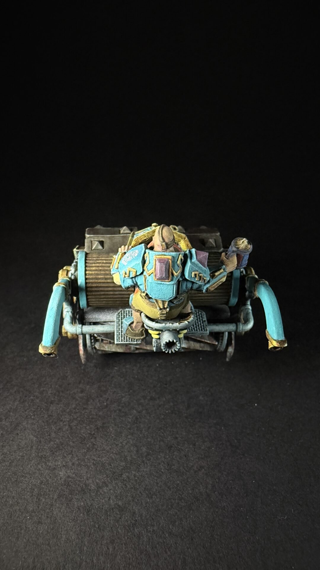 Rear view of a painted miniature sci‑fi combat crawler with teal armor and gold highlights, set against a black backdrop.