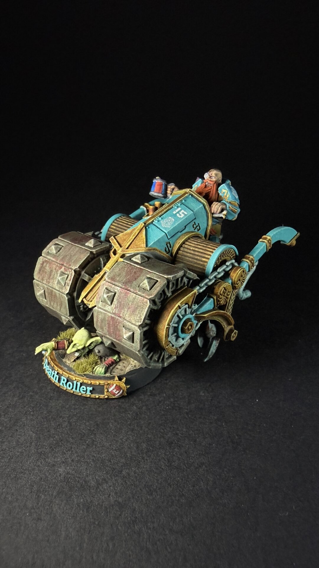 Painted Warhammer Death Roller miniature: teal and gold vehicle with a dwarf driver on a grassy diorama base, labeled Death Roller on the base banner.