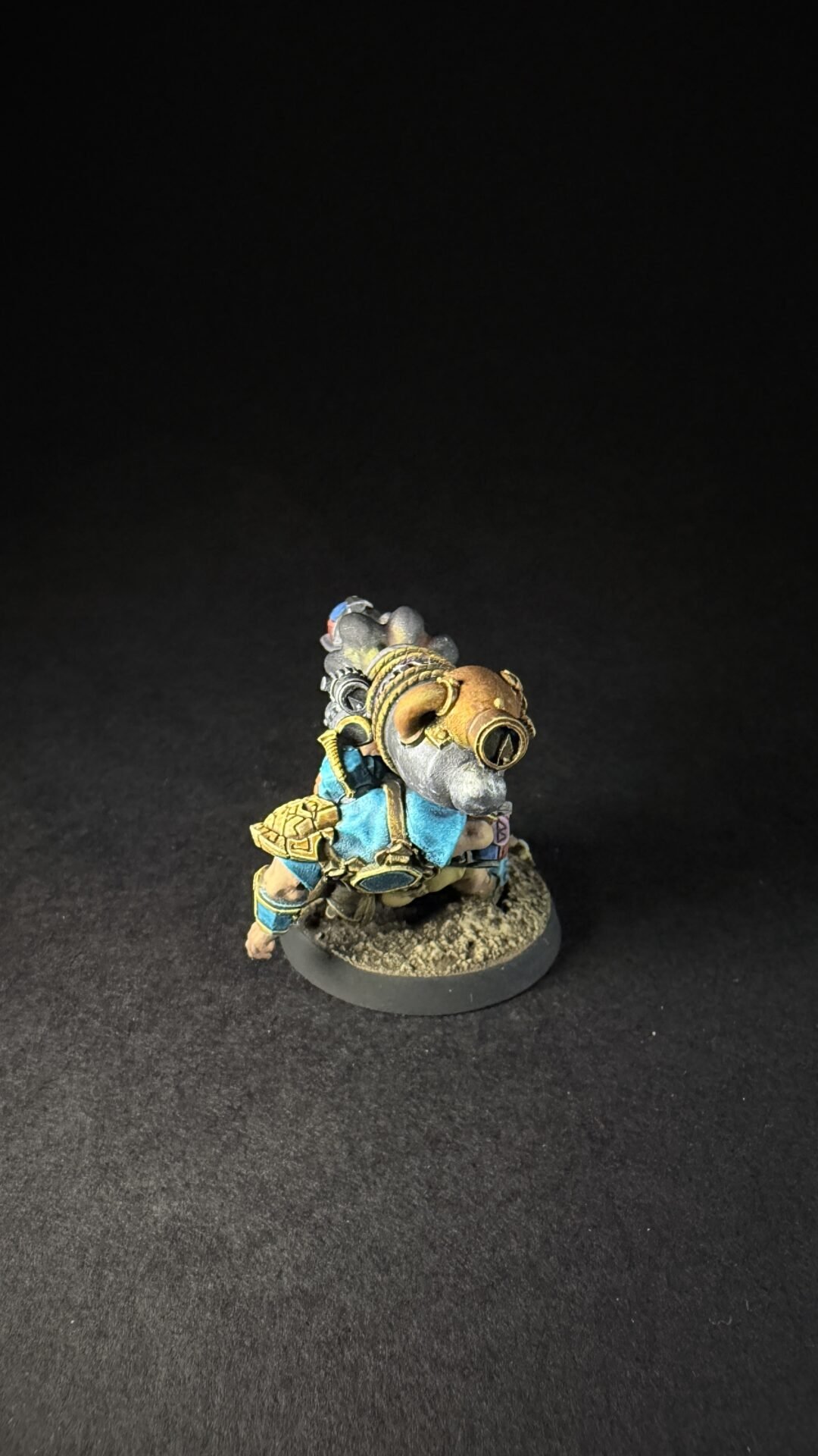 Painted fantasy miniature of a armored dwarf with steampunk goggles, blue and gold armor, standing on a textured base.