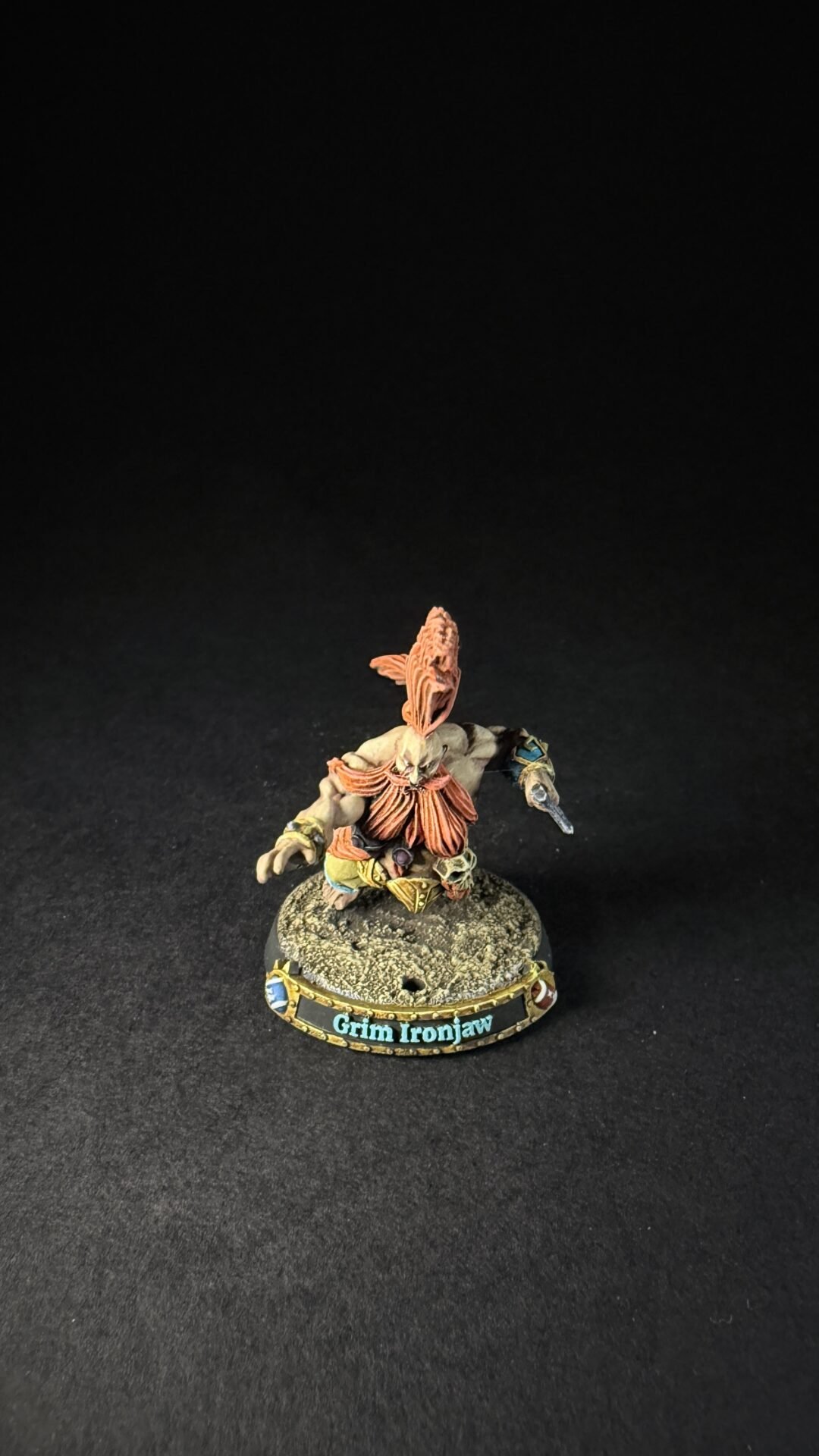 Small fantasy miniature Grim Ironjaw standing on a rocky base, painted armor with orange plumes and a weapon in hand.