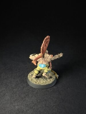 Front-facing miniature of a muscular fantasy orc with a tall orange feather headdress, outstretched arms, wearing a belt and tunic on a rocky base.