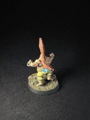 Back view of a painted tabletop miniature: muscular humanoid with long orange hair, wearing green pants, standing on a rocky base.