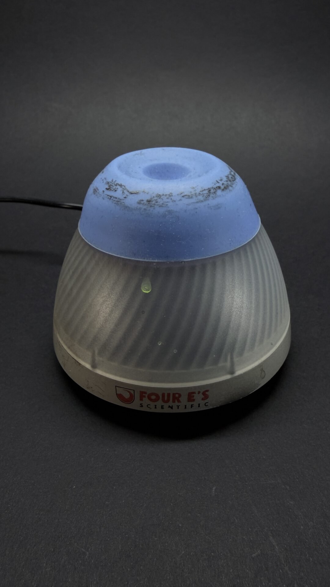 Blue silicone cap on a ribbed gray lab device base labeled Four E's Scientific; appears to be a small laboratory instrument component.